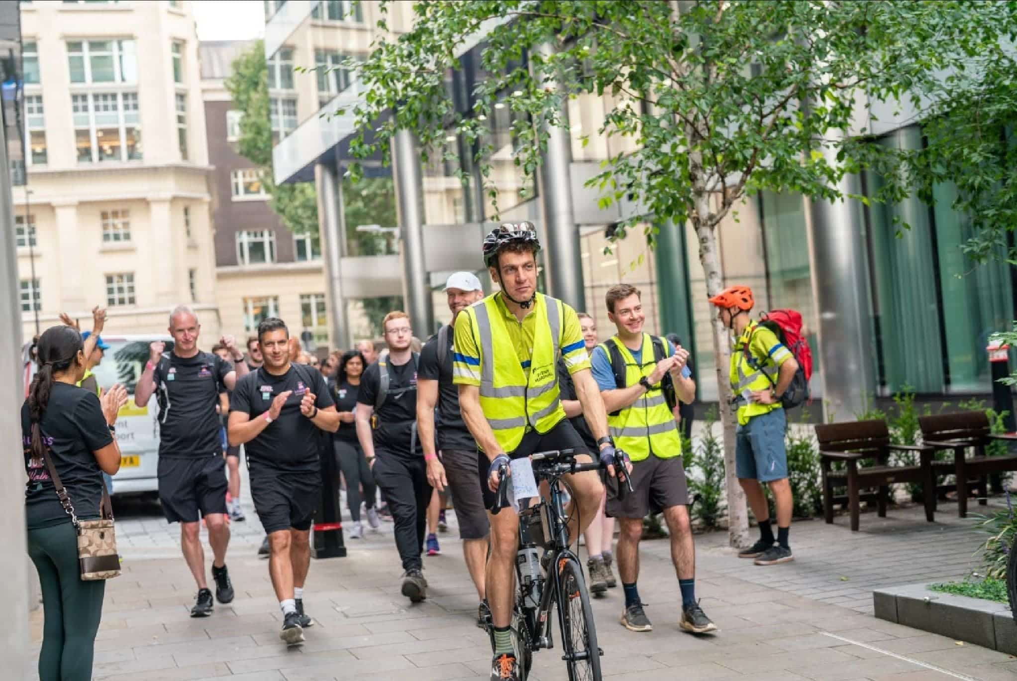 A man riding a bike with a ground of people following clapping